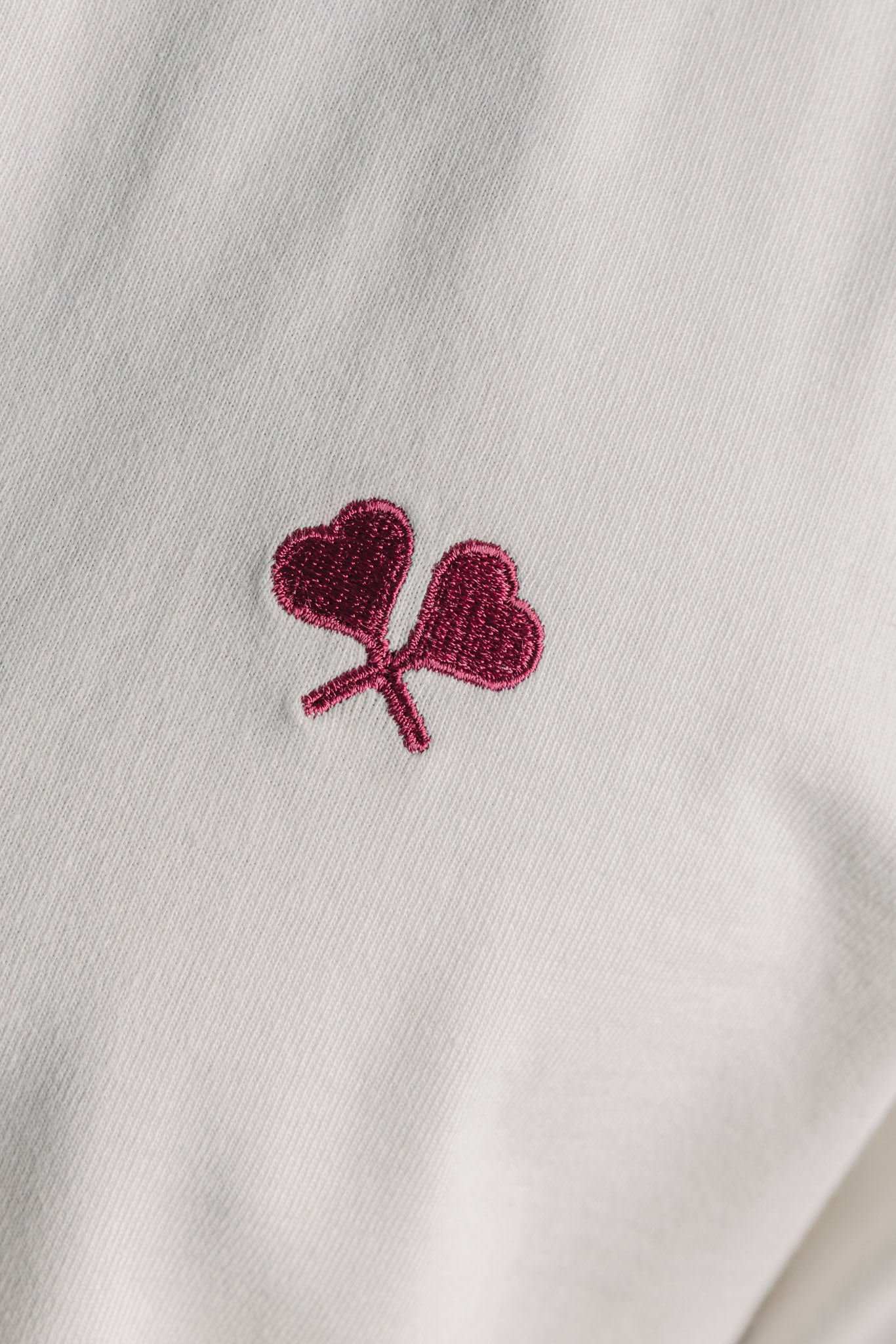 Close-up of subtle embroidered logo on white tennis tee fabric, showcasing quality detail.