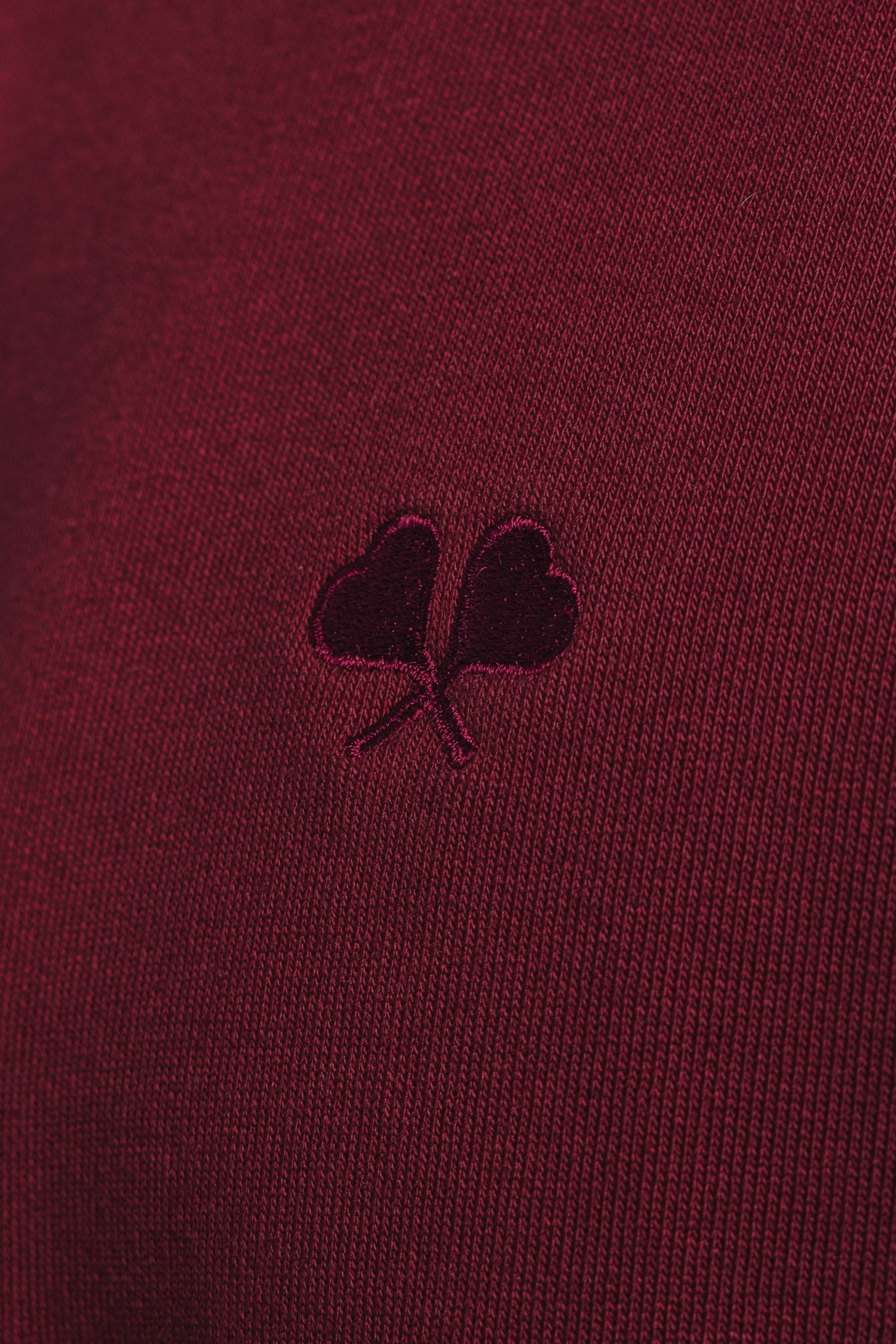 Macro shot of FL logo embroidery on burgundy sweater, highlighting fine stitch quality and fabric texture.