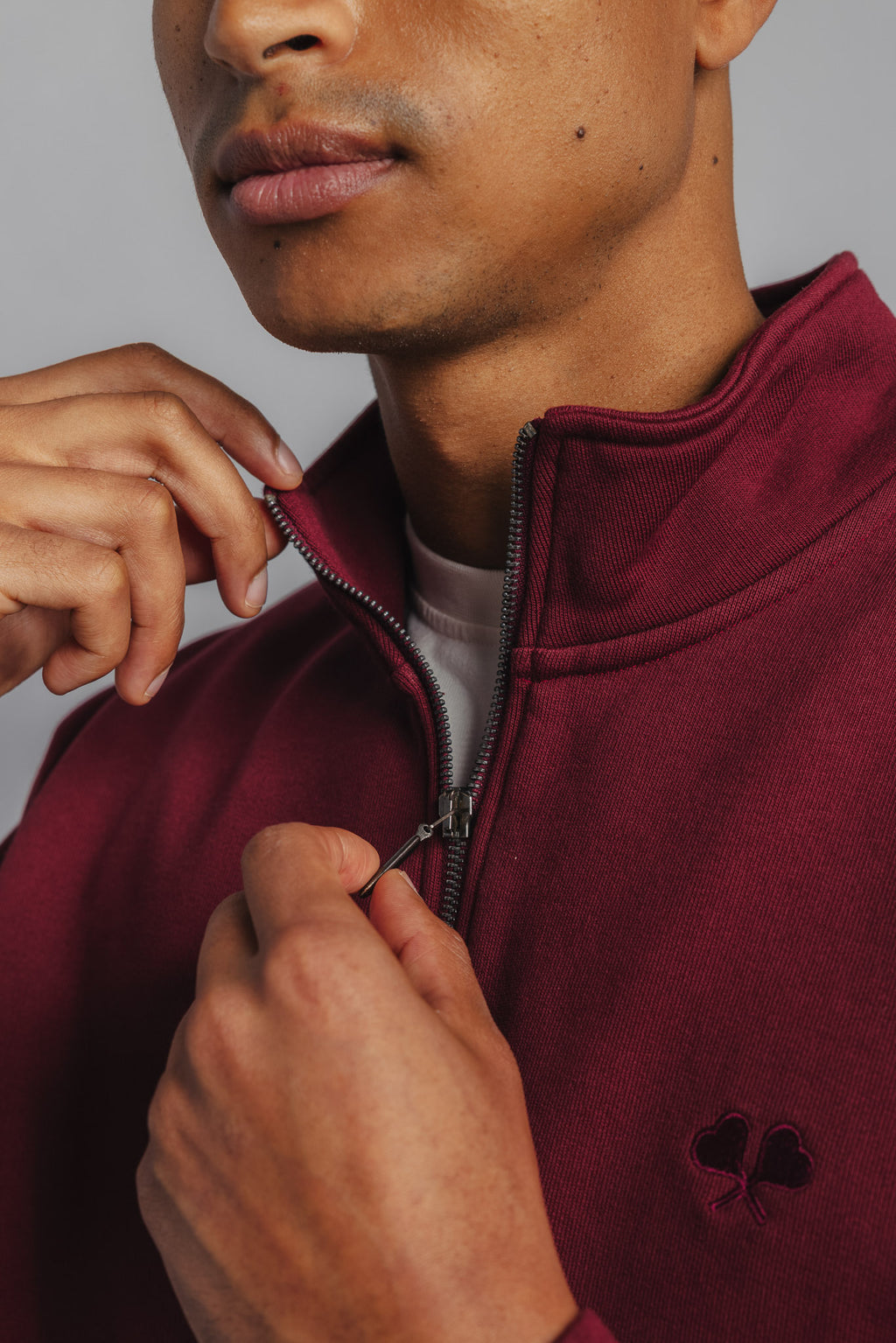Close-up of small FL embroidery on chest of burgundy tennis sweater, showcasing detailed tonal stitching.