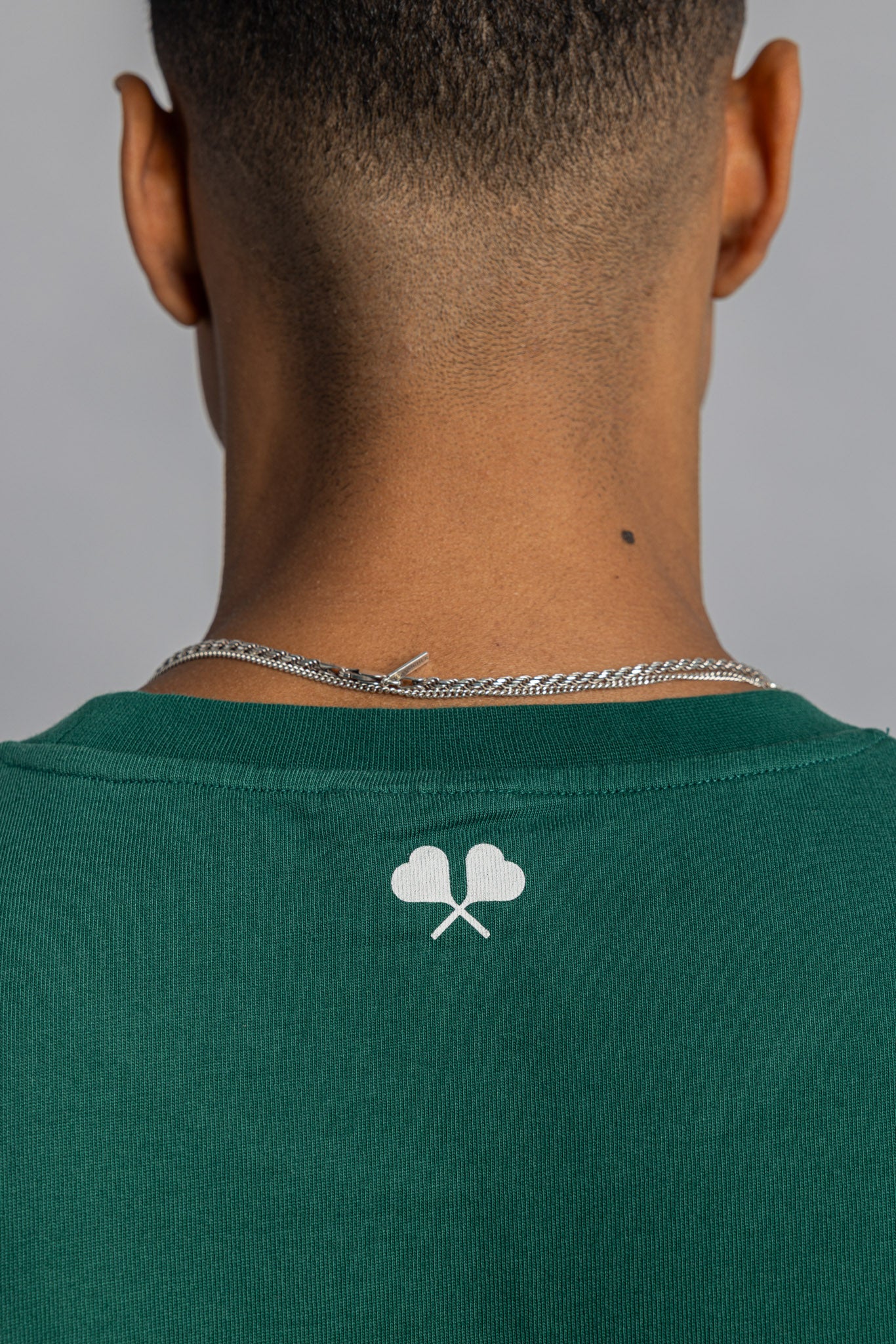 Close-up of heart racquet print on upper back of court green tee, below neckline.