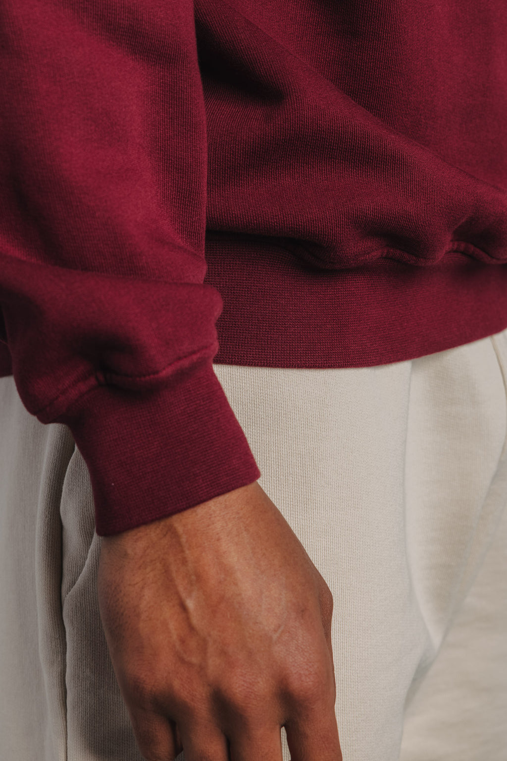 Close-up of sleeve on burgundy tennis sweater, highlighting ribbed cuff and soft organic cotton texture.