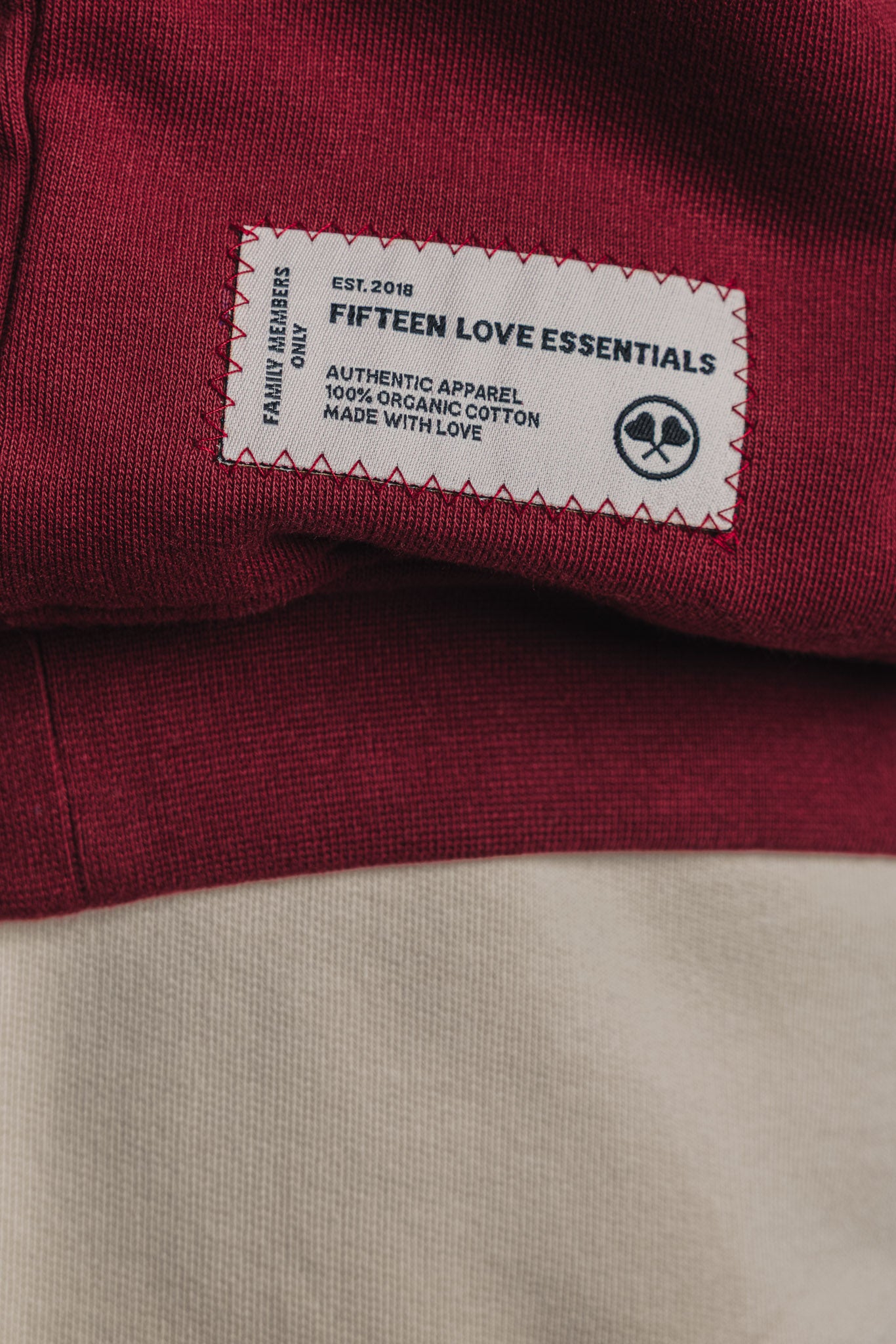 Close-up of tonal zig-zag stitched patch detail on burgundy tennis sweater, located on the lower back.