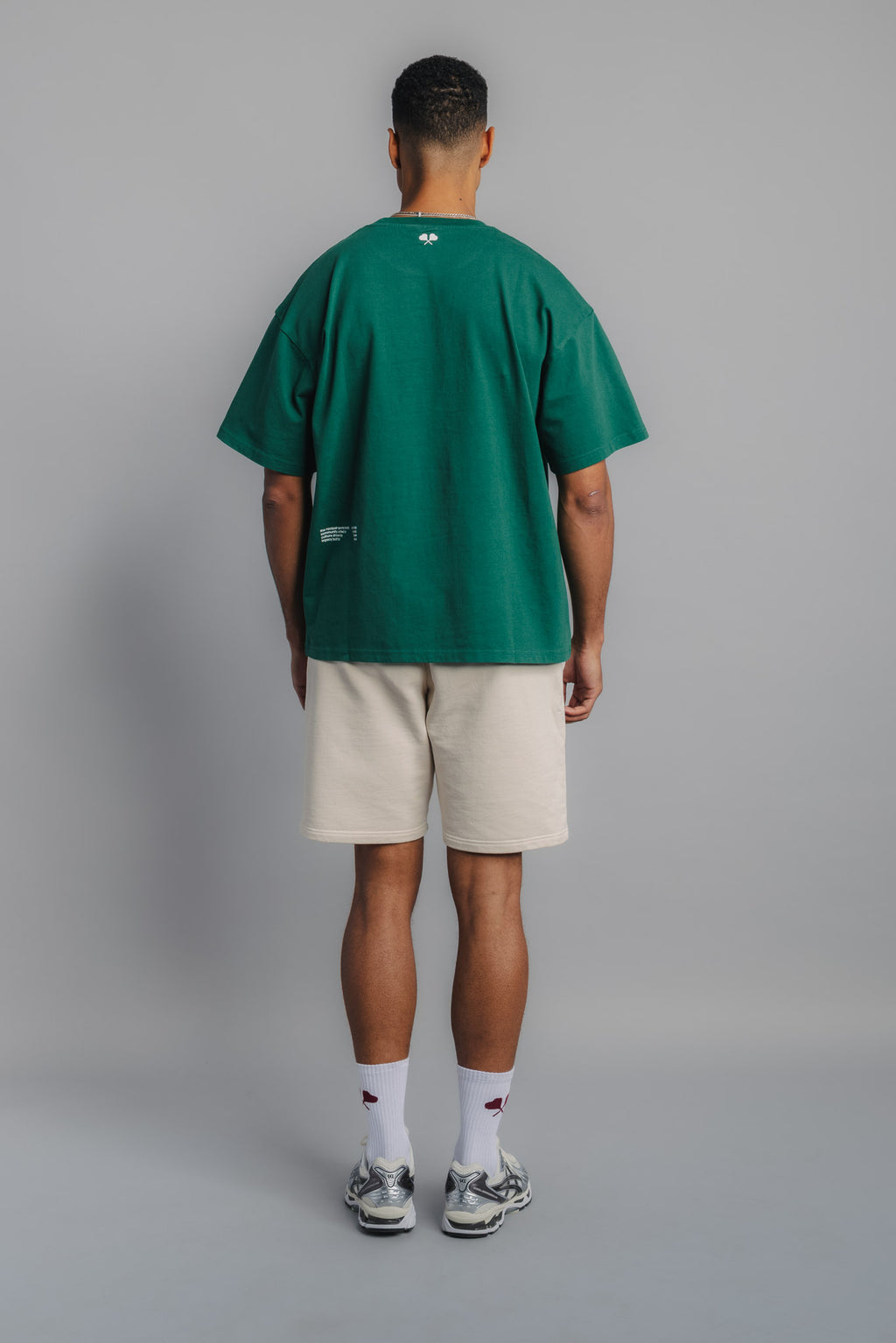 Back view of male model in court green tee with small heart racquet graphic below neckline.