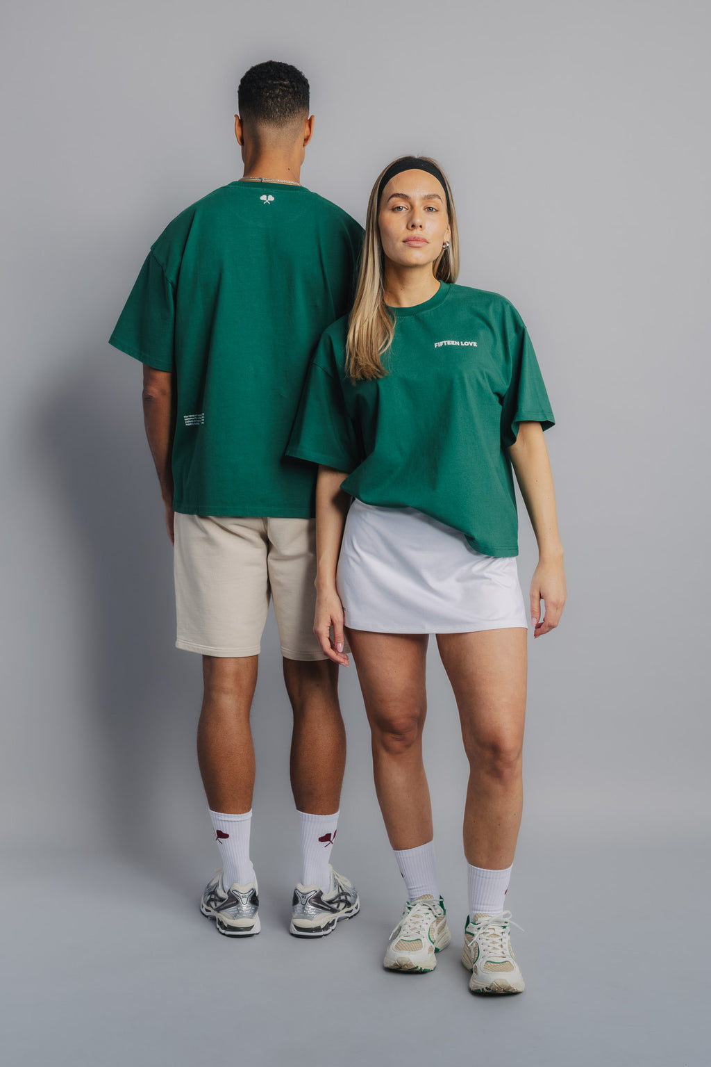 Tennis models in court green tee, one front-facing with FL chest embroidery, the other showing heart racquet backprint.
