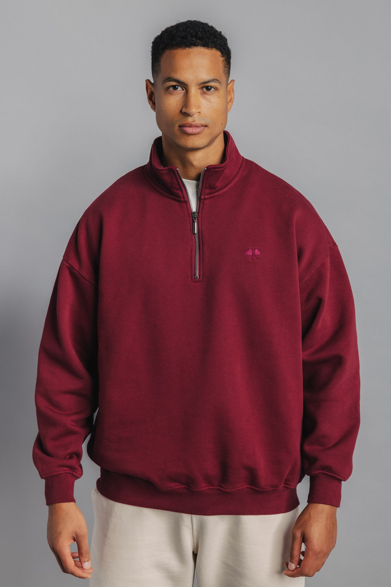Male model wearing burgundy tennis sweater, front view showing small FL chest embroidery and high collar.