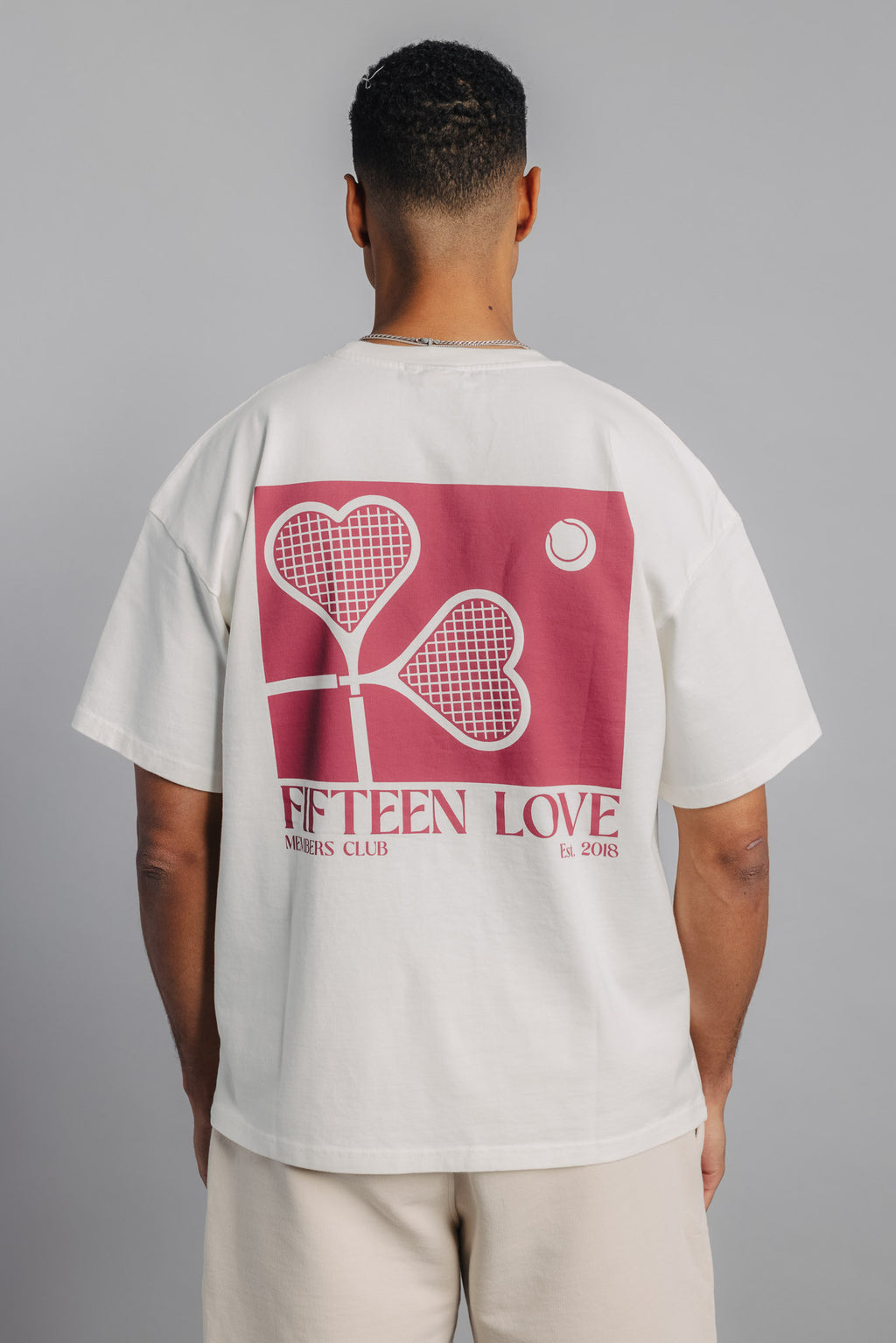 Male tennis model showing back of white tennis tee with large heart racquet print.